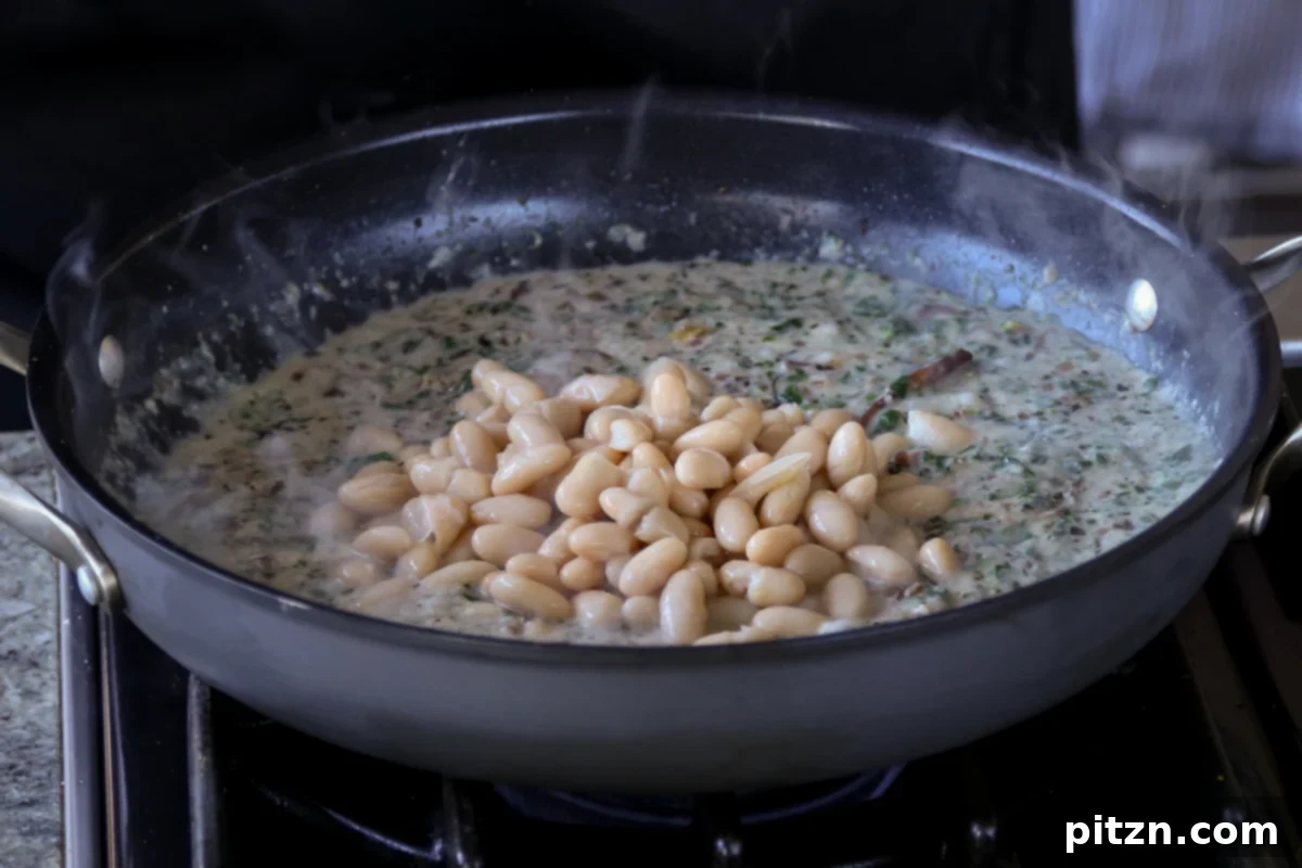 Drained white beans being stirred into the rich and creamy Kali Mirch sauce in the pan, ready to simmer and absorb flavors.