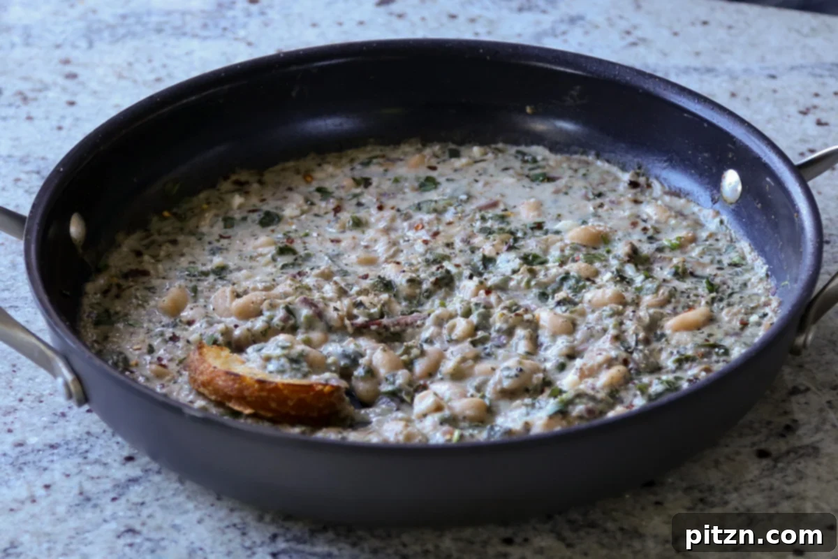 A final shot of the completed Kali Mirch Beans in the pan, garnished and ready to be served, with a piece of sourdough bread for dipping.