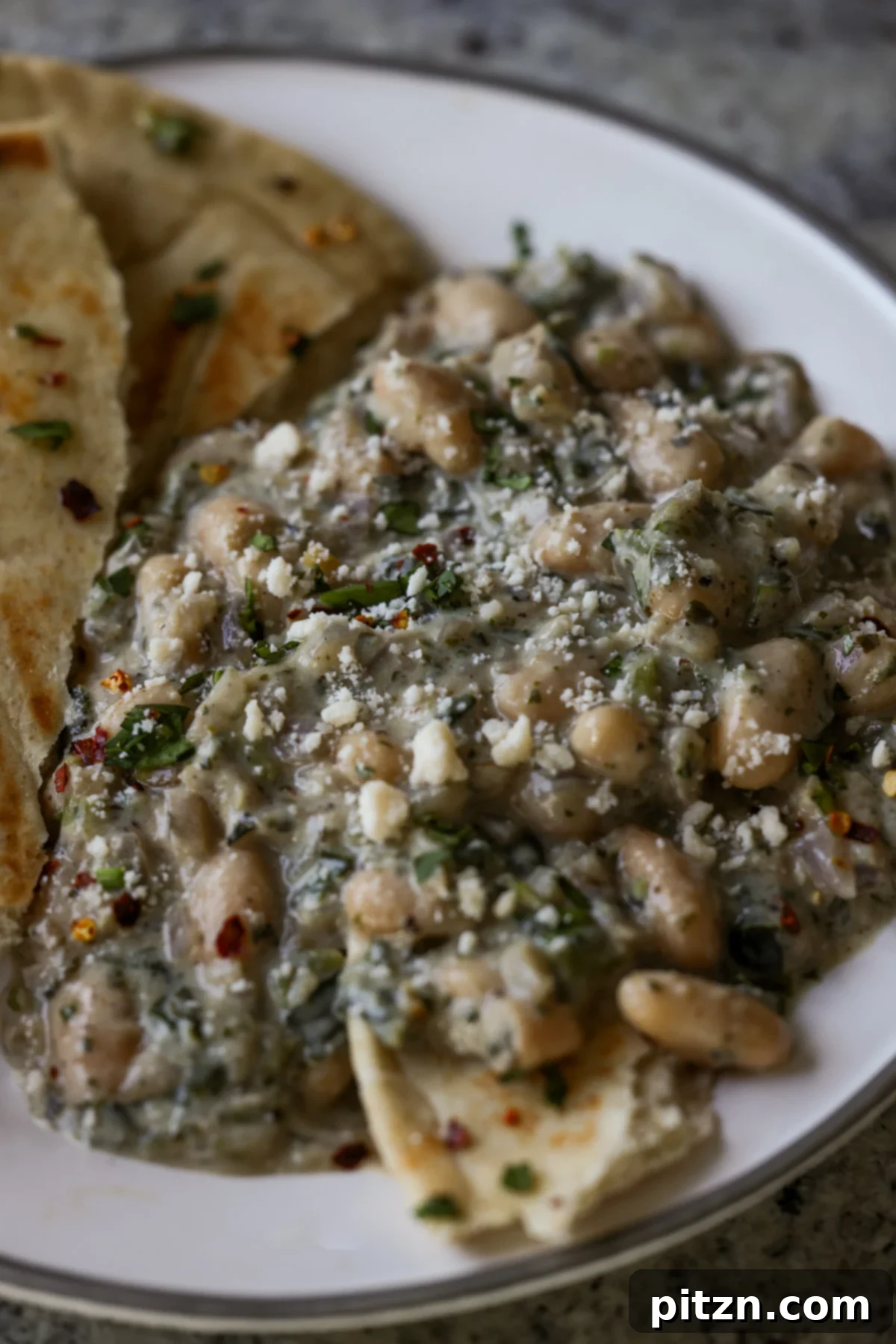 Kali Mirch Beans served on a white plate with a side of Indian flatbread, garnished with fresh cilantro and black pepper.