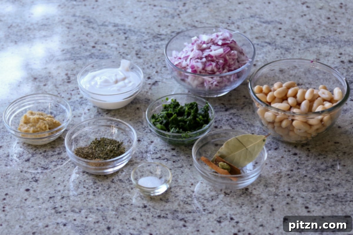 Bowls filled with individual spices and ingredients for Kali Mirch Beans, including whole spices, ground pepper, onions, and beans, arranged on a kitchen counter.
