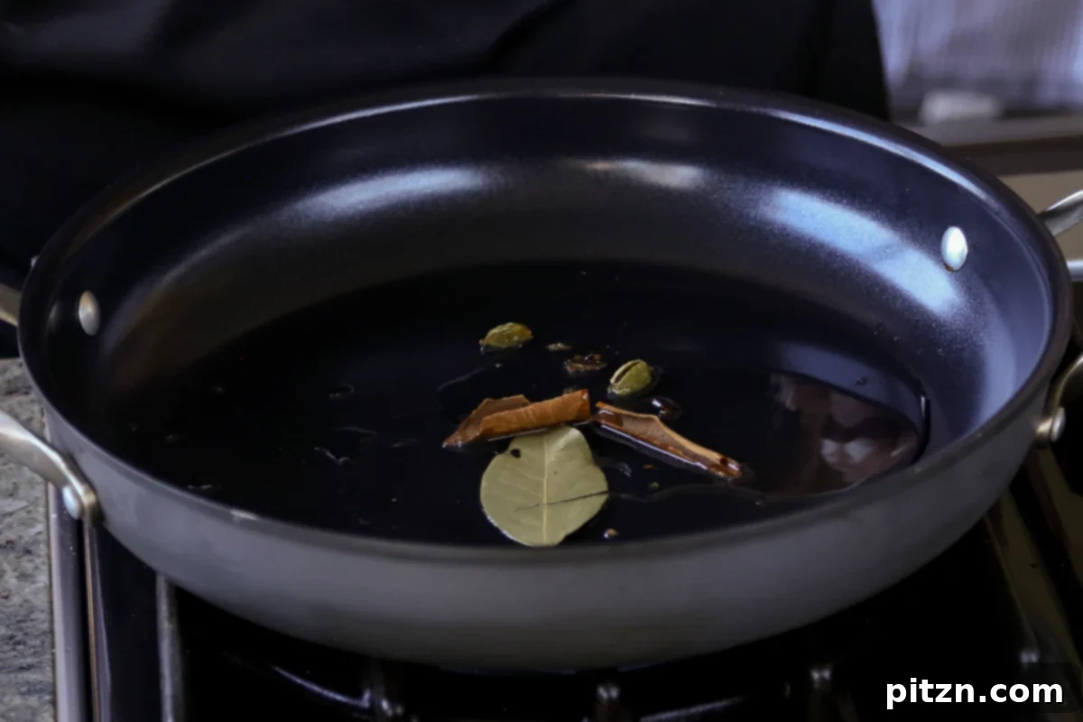 Whole spices, including cloves, bay leaf, cardamom, and cinnamon stick, gently toasting in oil in a skillet.