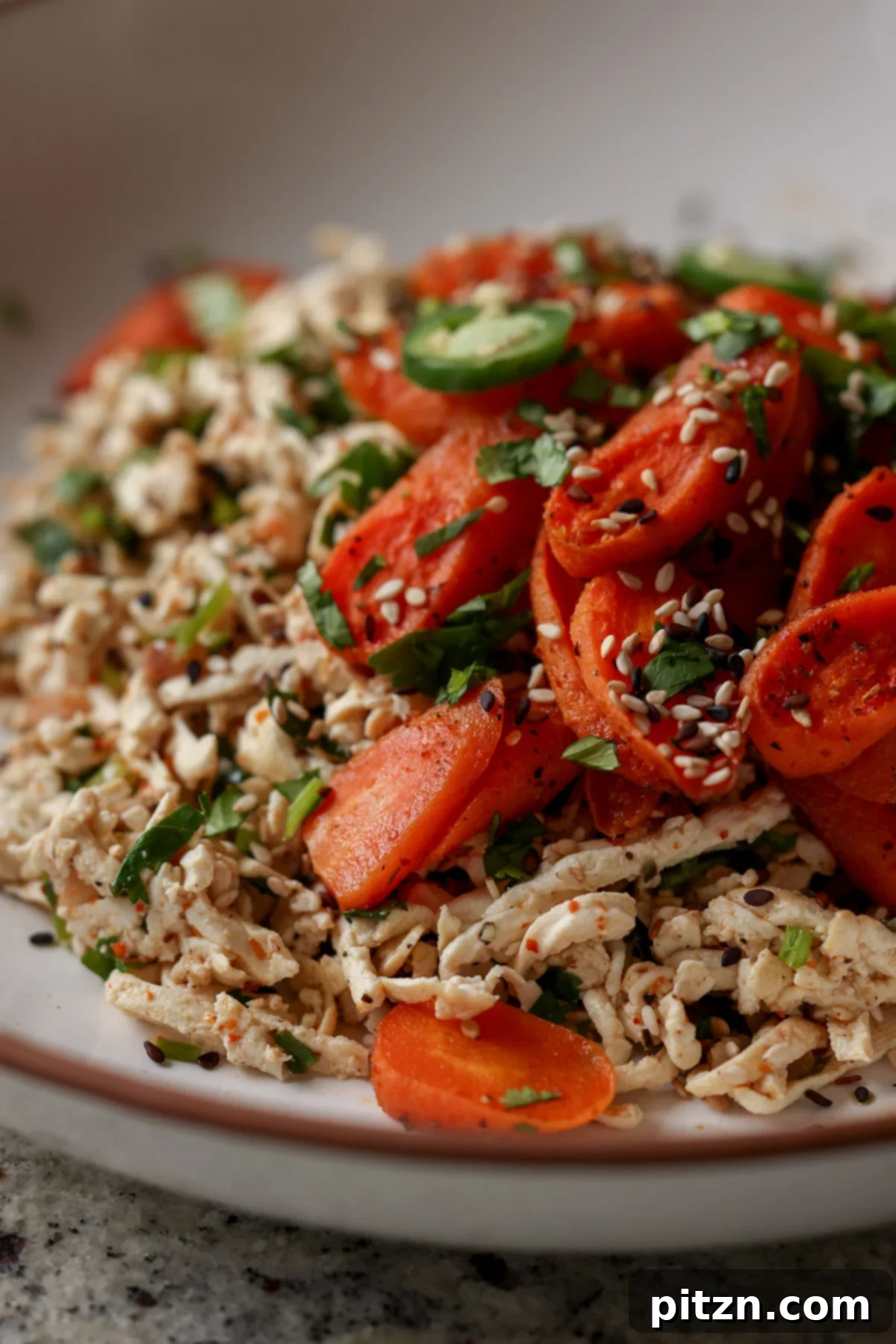 Close-up of shredded tofu topped with vibrant roasted carrots in a bowl, ready to be enjoyed.