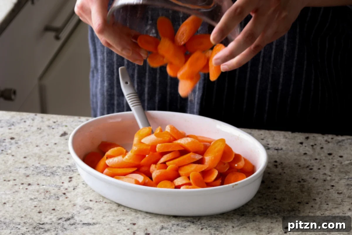Adding diagonally sliced carrots to a baking pan for roasting.