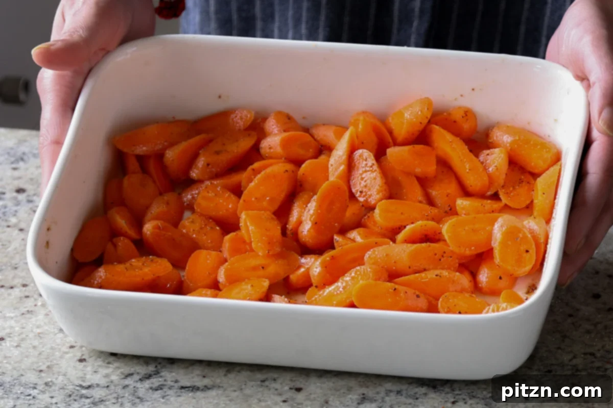 Carrots evenly spread in the pan, seasoned and ready for roasting.