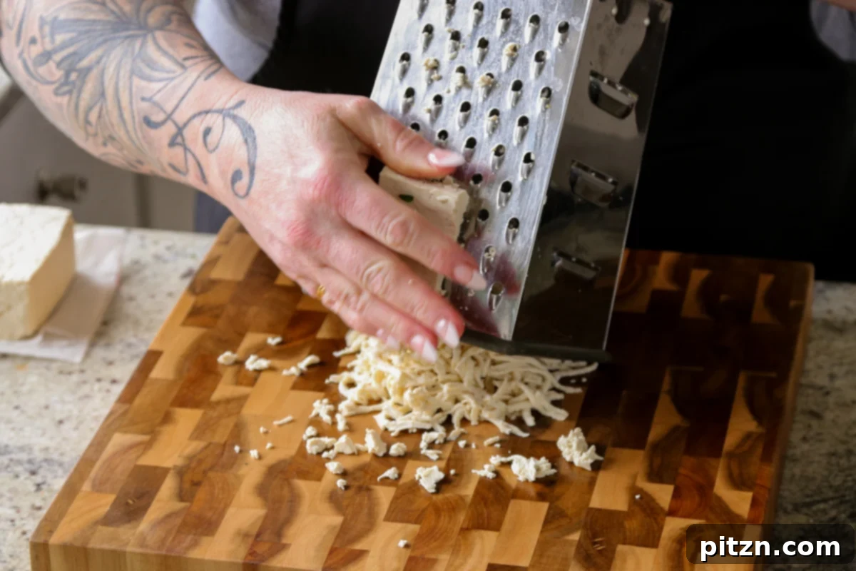Grating a block of pressed tofu with a box grater to create shredded tofu.