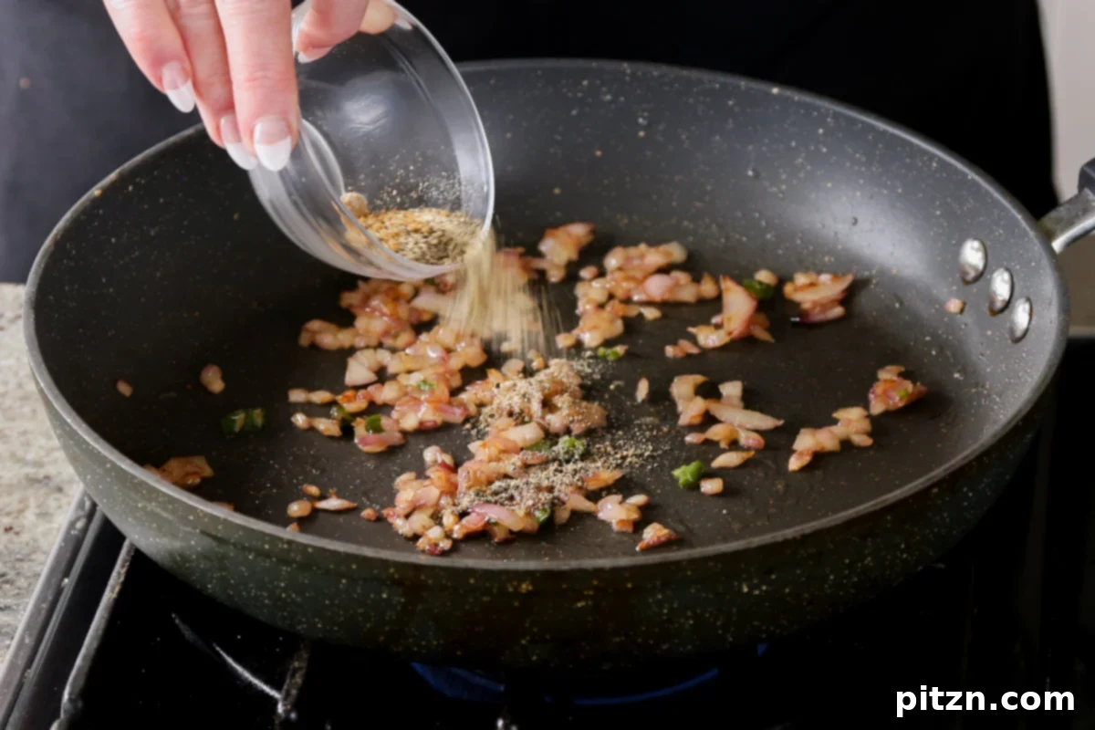 Adding spices to the sautéed onion in the pan for the tofu mixture.