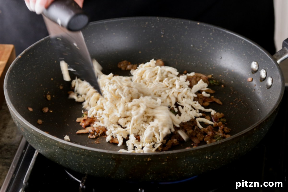 Adding shredded tofu to the pan with cooked onion and spices.