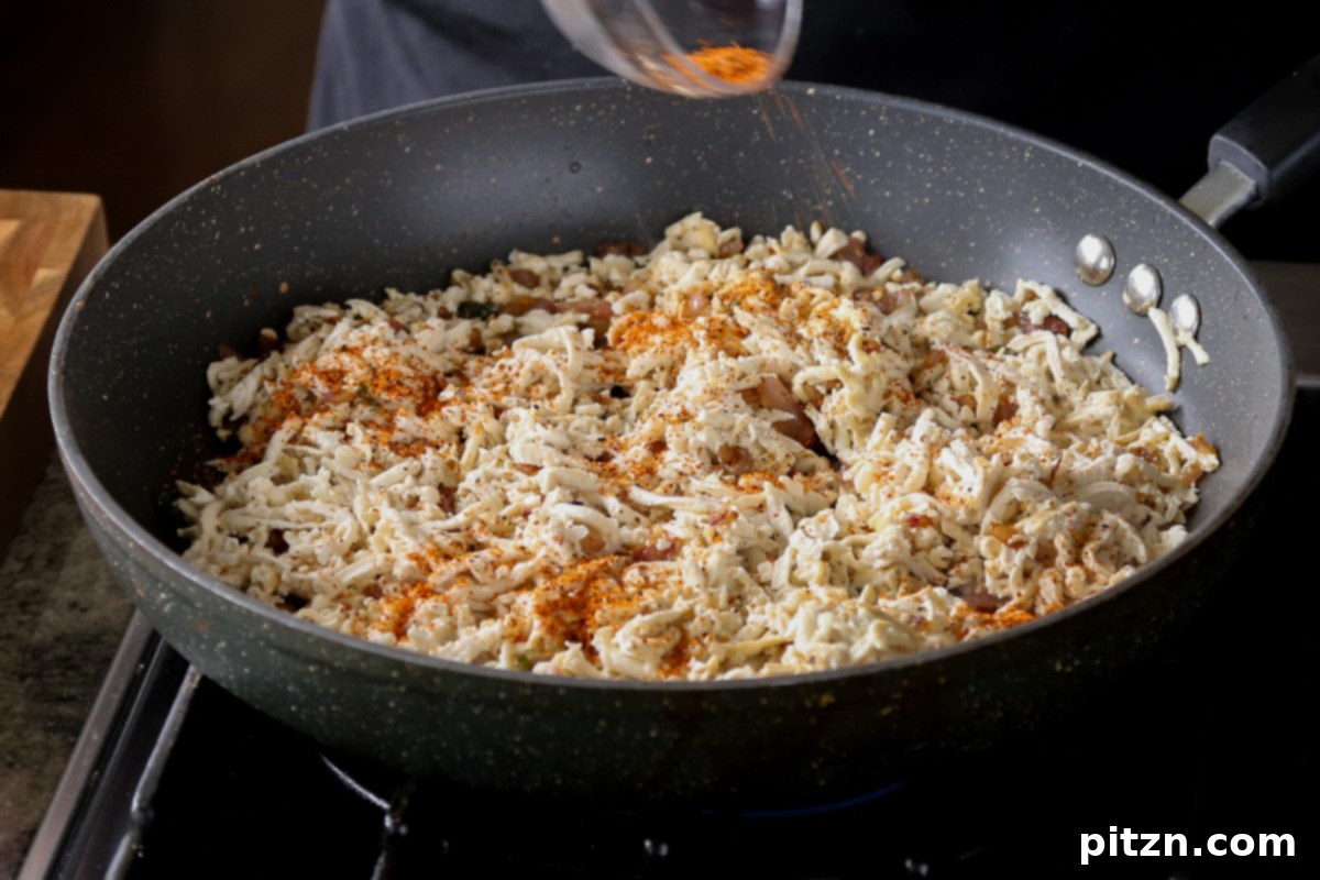 Mixing fresh cilantro into the cooked shredded tofu in the pan.