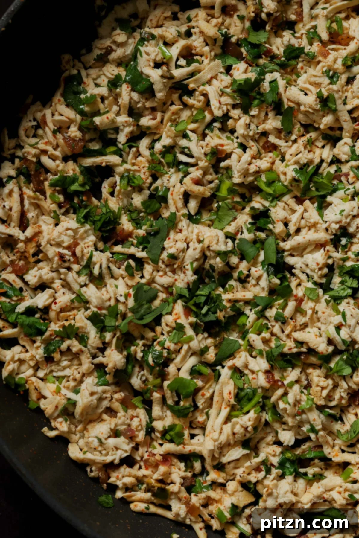 Close-up of cilantro lime shredded tofu simmering in a pan, highlighting the spices and herbs.