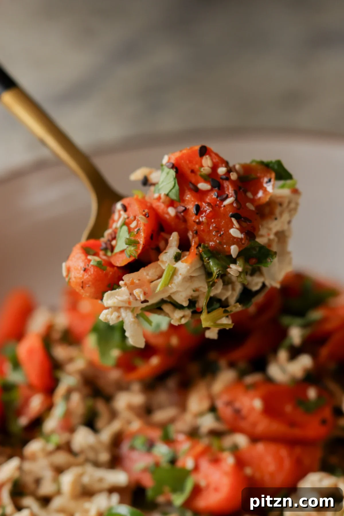 A spoon lifting a bite of shredded tofu topped with roasted carrots, showing the vibrant colors of the dish.