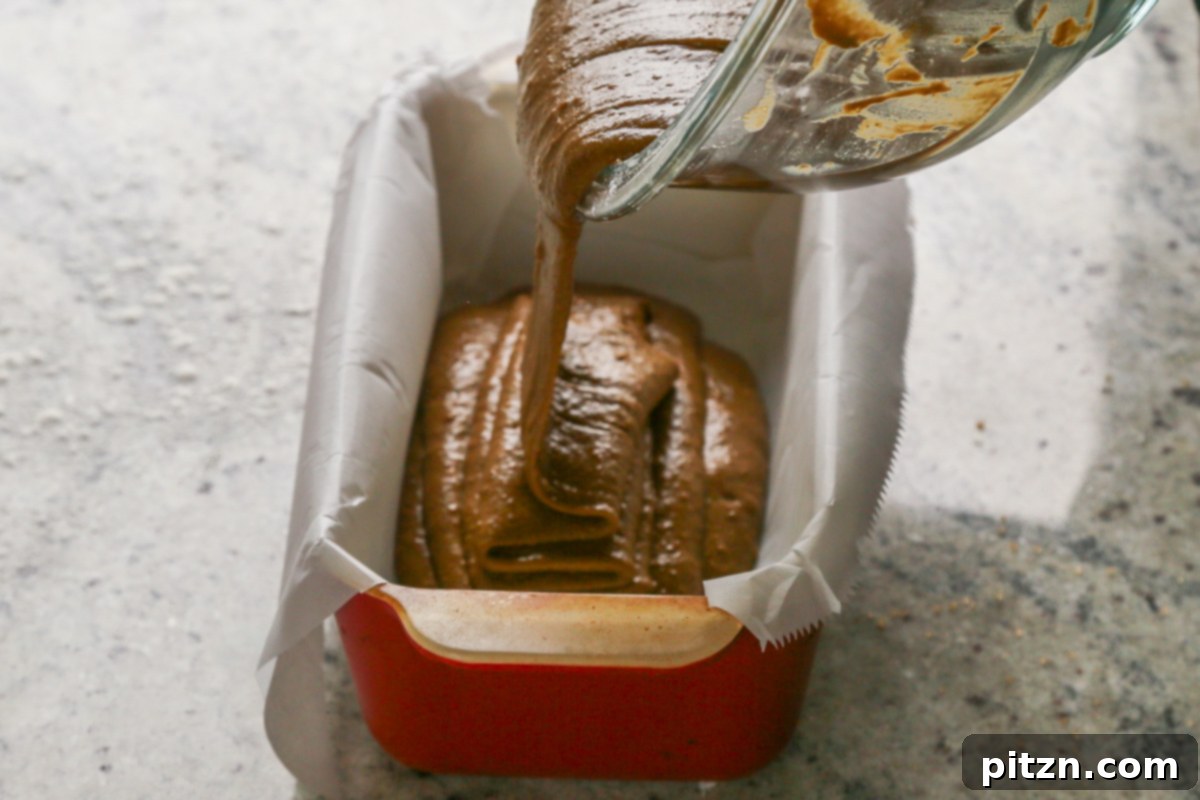 Luscious Triple Ginger Vegan Gingerbread Cake 16 Thick vegan gingerbread cake batter being poured into a parchment-lined loaf pan, ready for baking.