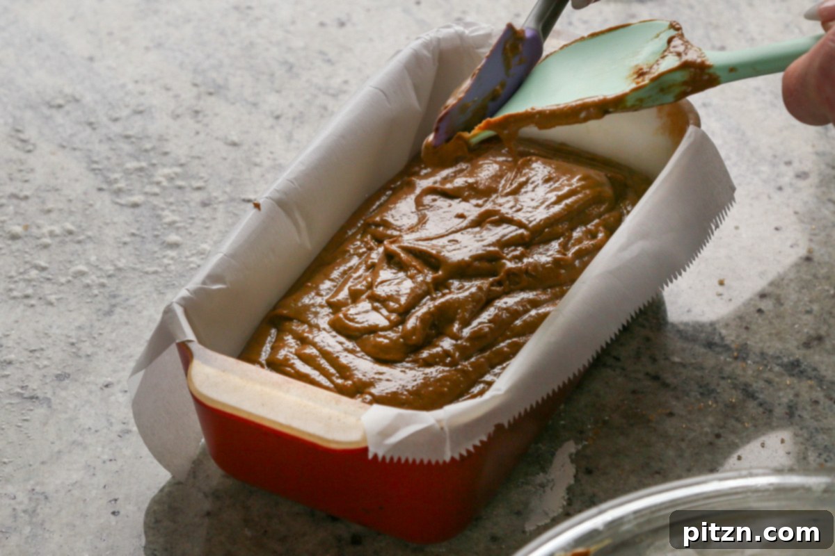 Luscious Triple Ginger Vegan Gingerbread Cake 17 A spatula smoothing out the top of the vegan gingerbread cake batter in a loaf pan, preparing it for an even bake.