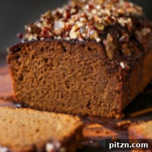 A perfectly baked vegan gingerbread cake on a cutting board, with a slice removed to show its moist interior. The cake is topped with a generous ginger glaze and chopped nuts.