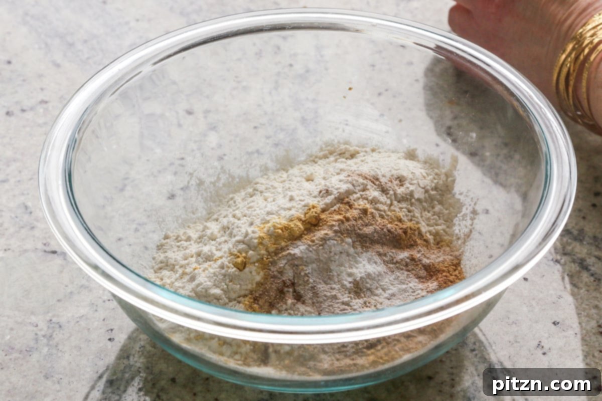 Luscious Triple Ginger Vegan Gingerbread Cake 9 A close-up of dry ingredients including flour, spices, and leavening agents being mixed together in a large white bowl with a whisk.