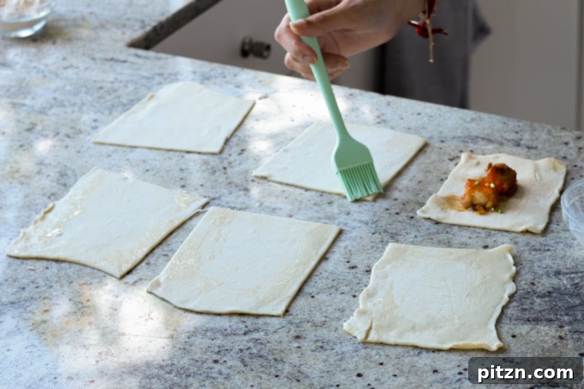 Flaky Indo Chinese Chilli Garlic Tofu Parcels 22 A pastry brush applying the maple-non-dairy milk mixture to the edges of a puff pastry square.
