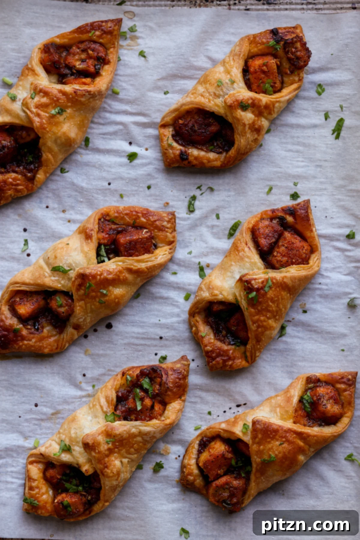 Flaky Indo Chinese Chilli Garlic Tofu Parcels 4 Baked chilli garlic tofu puff pastry parcels arranged neatly on a parchment-lined baking sheet, showcasing their golden-brown color and crispy texture.