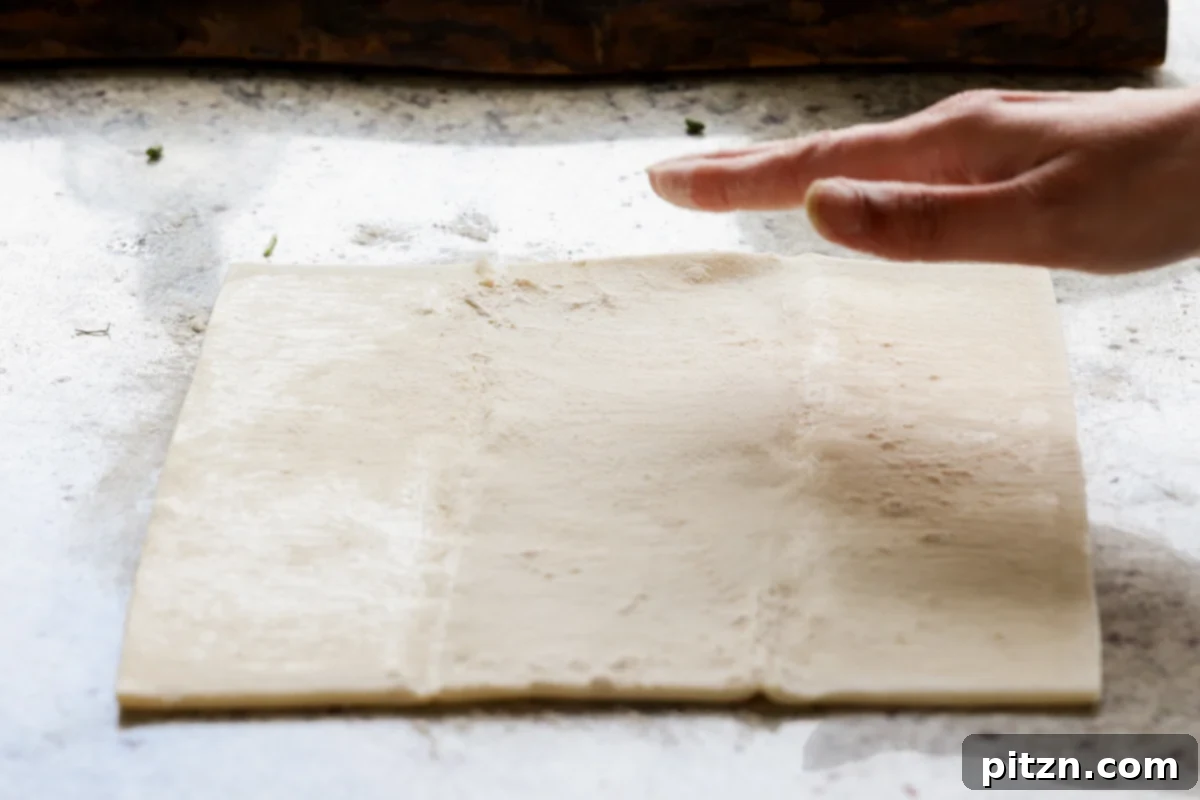 Vegan Jalapeño Popper Pinwheels 13 A hand lightly dusting a puff pastry sheet with flour on a counter before rolling.