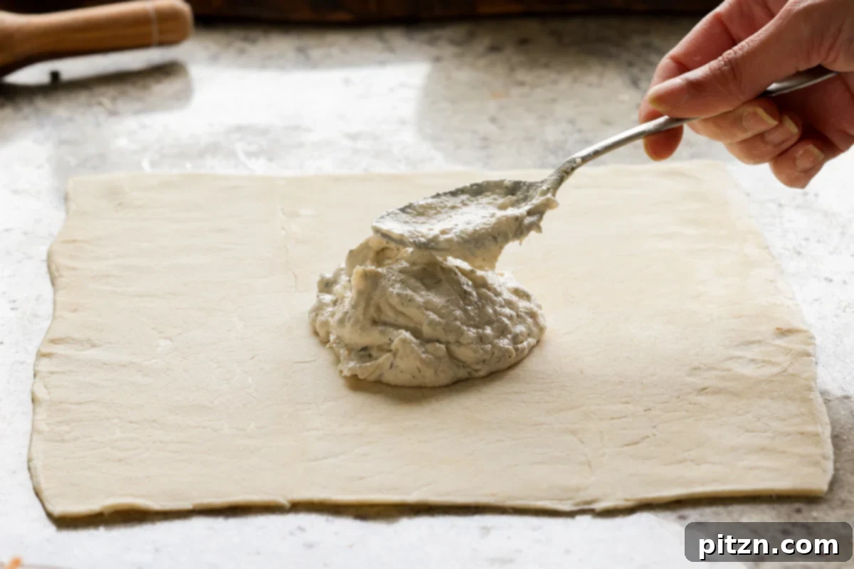 Vegan Jalapeño Popper Pinwheels 15 A spoon meticulously applying a generous amount of jalapeño popper dip onto the rolled puff pastry sheet.