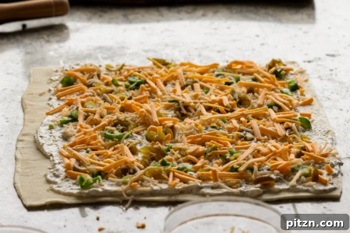 Vegan Jalapeño Popper Pinwheels 18 Various vegan cheeses, including cheddar shreds and parmesan, being added evenly over the jalapeño popper filling on the puff pastry.