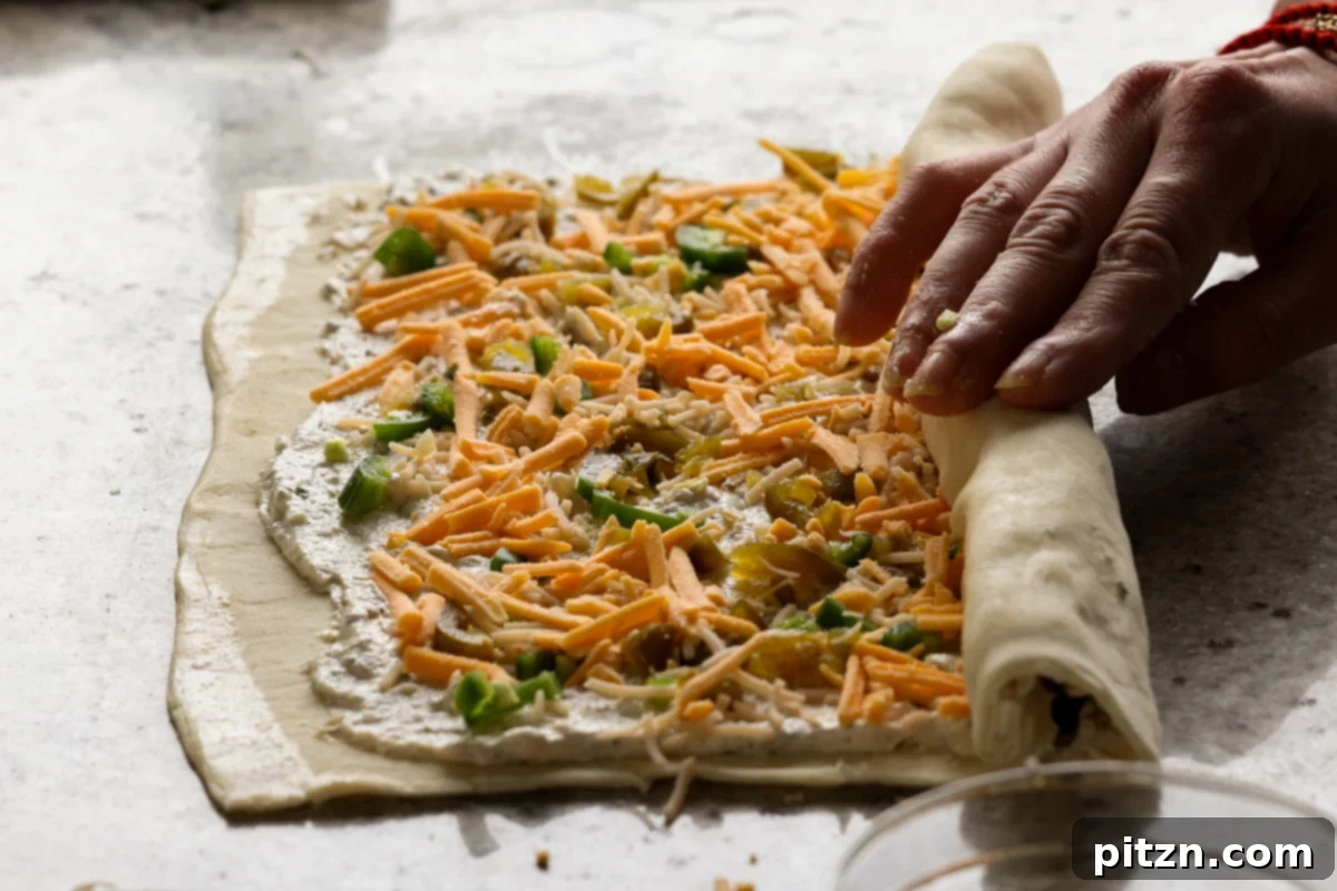 Vegan Jalapeño Popper Pinwheels 19 A close-up of hands carefully rolling up the puff pastry sheet filled with jalapeño popper ingredients to form a log.