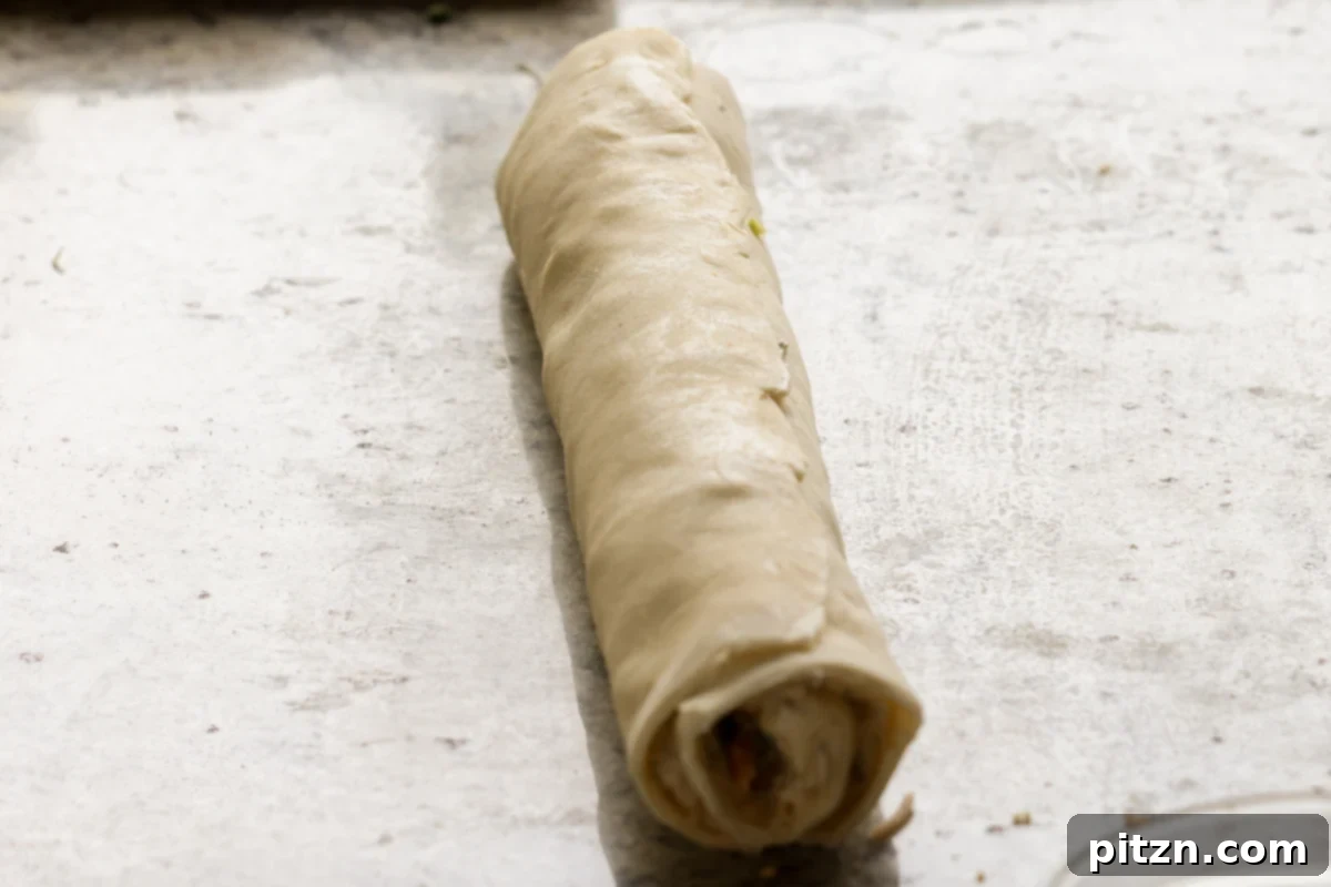 Vegan Jalapeño Popper Pinwheels 20 The rolled-up jalapeño popper puff pastry log, ready for chilling and slicing, sitting on a parchment-lined surface.