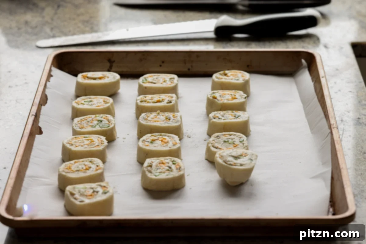 Vegan Jalapeño Popper Pinwheels 23 Neatly sliced jalapeño popper pinwheels arranged on a parchment-lined baking sheet, ready for the oven.