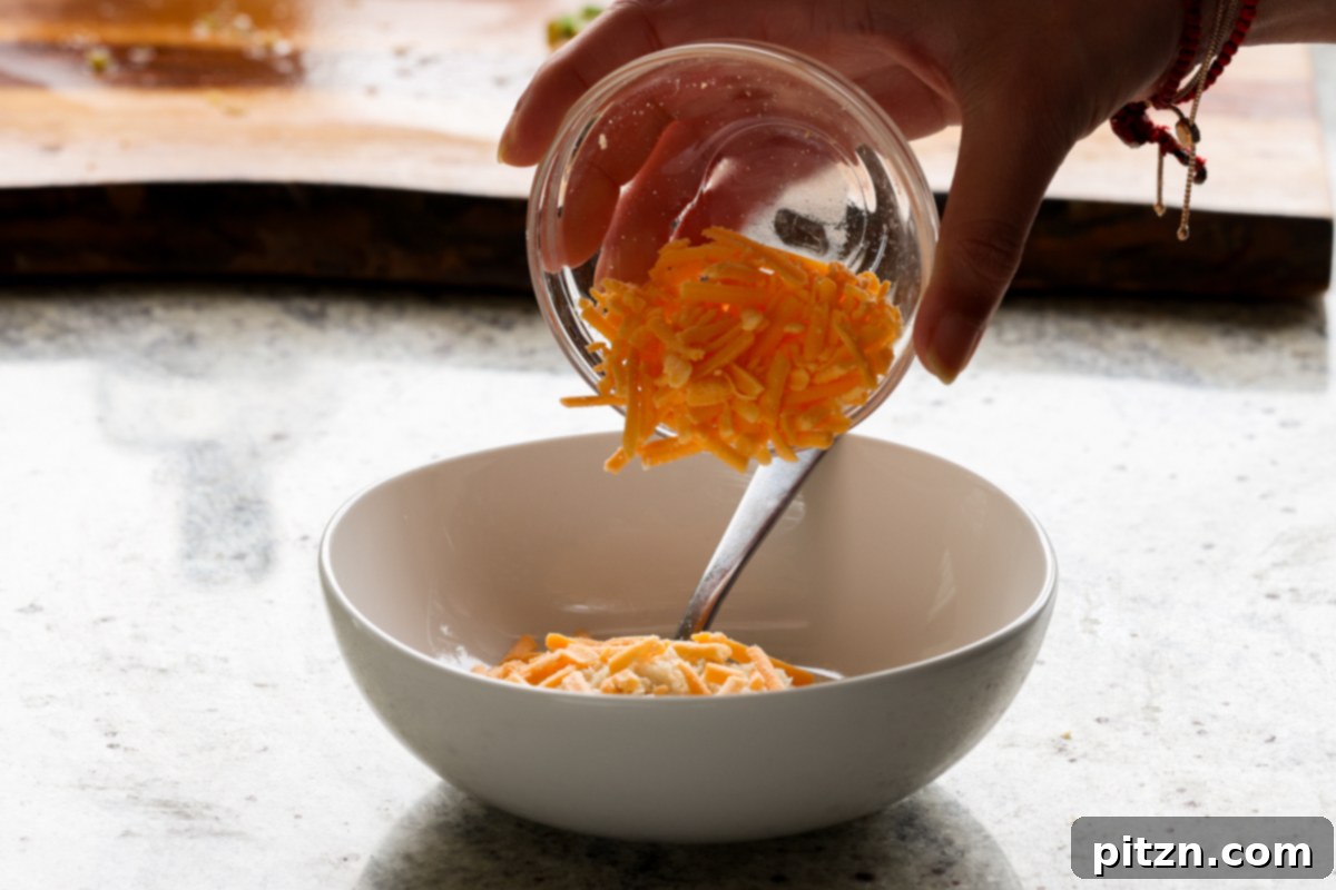 Vegan Jalapeño Popper Pinwheels 24 Vegan cheddar shreds being carefully added to a small bowl, part of the topping ingredients for the pinwheels.
