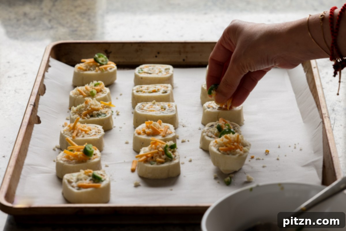 Vegan Jalapeño Popper Pinwheels 27 A hand evenly sprinkling the crispy, cheesy topping mixture over the raw jalapeño popper pinwheels on a baking sheet.