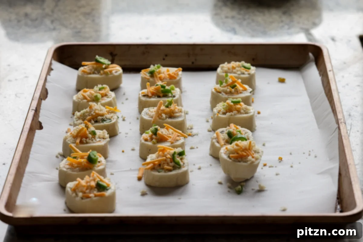 Vegan Jalapeño Popper Pinwheels 28 Jalapeño popper pinwheels, topped with breadcrumbs and cheese, neatly arranged on a baking sheet, ready to go into the oven.