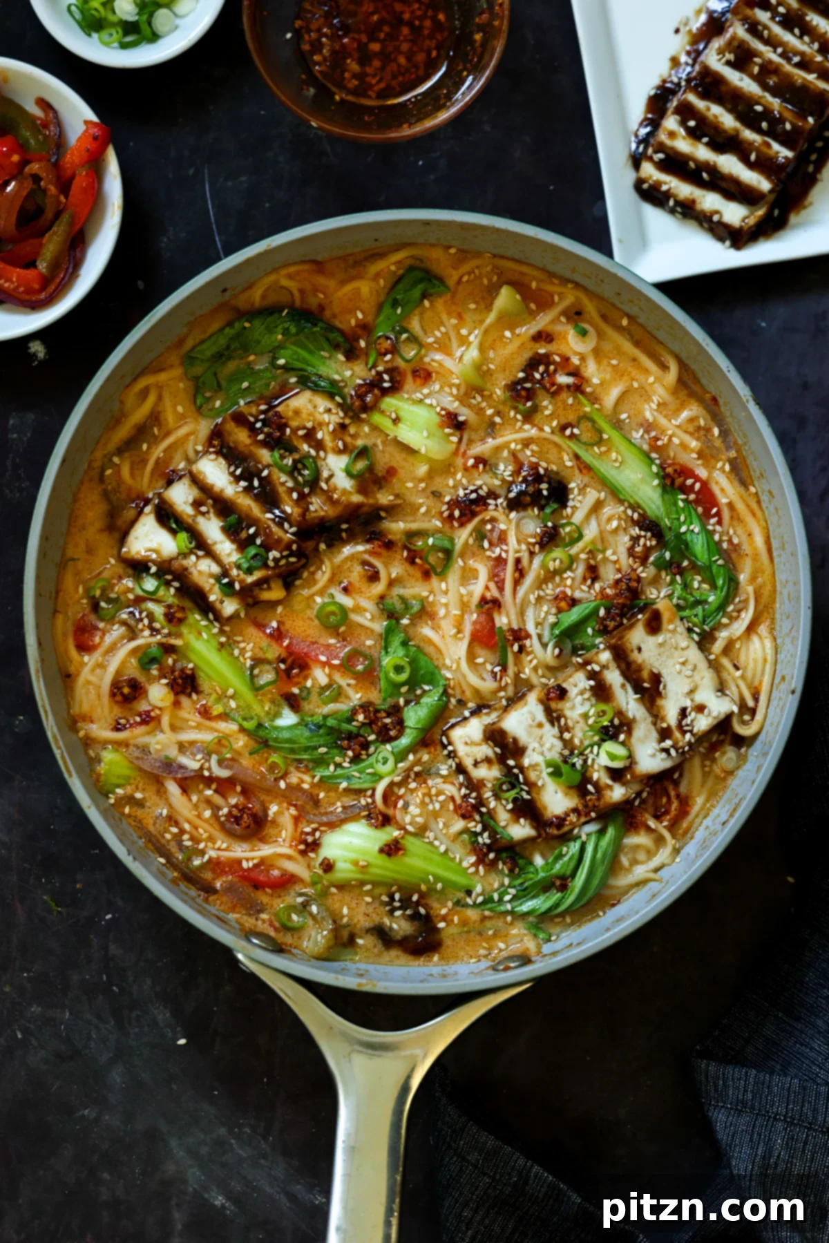 panful of creamy tahini ramen with teriyaki tofu on top, garnished with green onions and sesame seeds