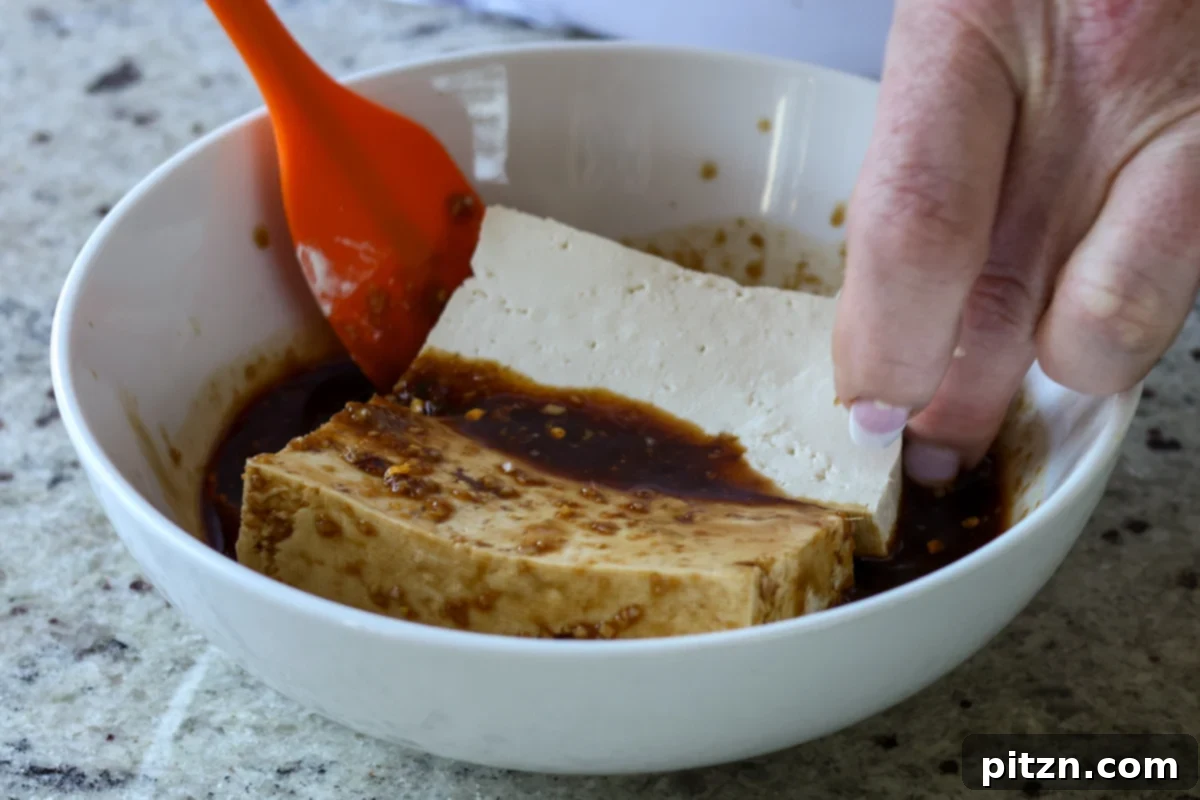 thick slabs of tofu being submerged into the savory teriyaki marinade in a shallow bowl