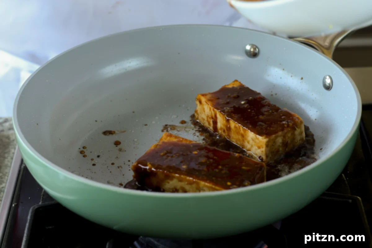 more teriyaki sauce being added to the pan with the tofu, creating a thicker glaze