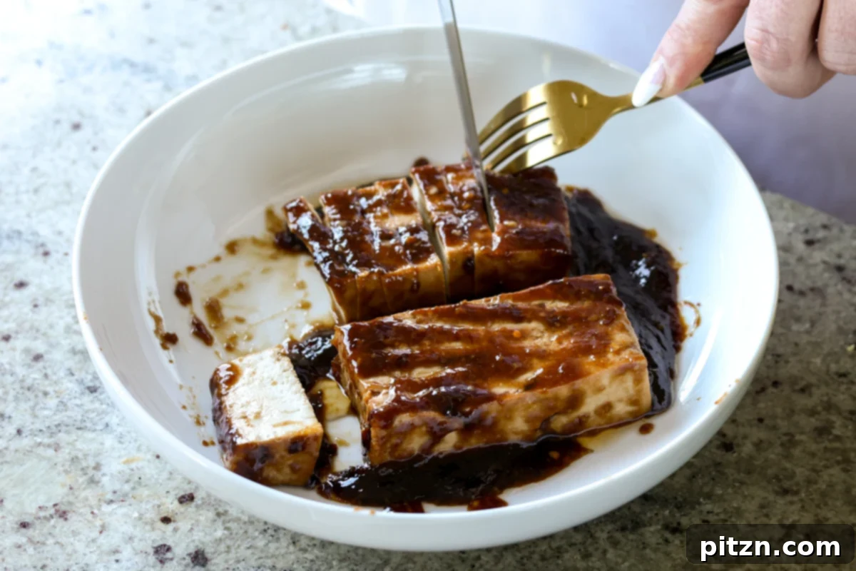 hands carefully slicing glazed teriyaki tofu slabs into even 1/4-inch thick strips on a cutting board