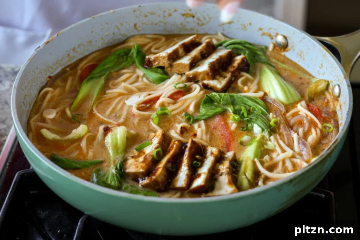 sliced teriyaki tofu being arranged artistically on top of the cooked tahini ramen in the pan, ready for serving