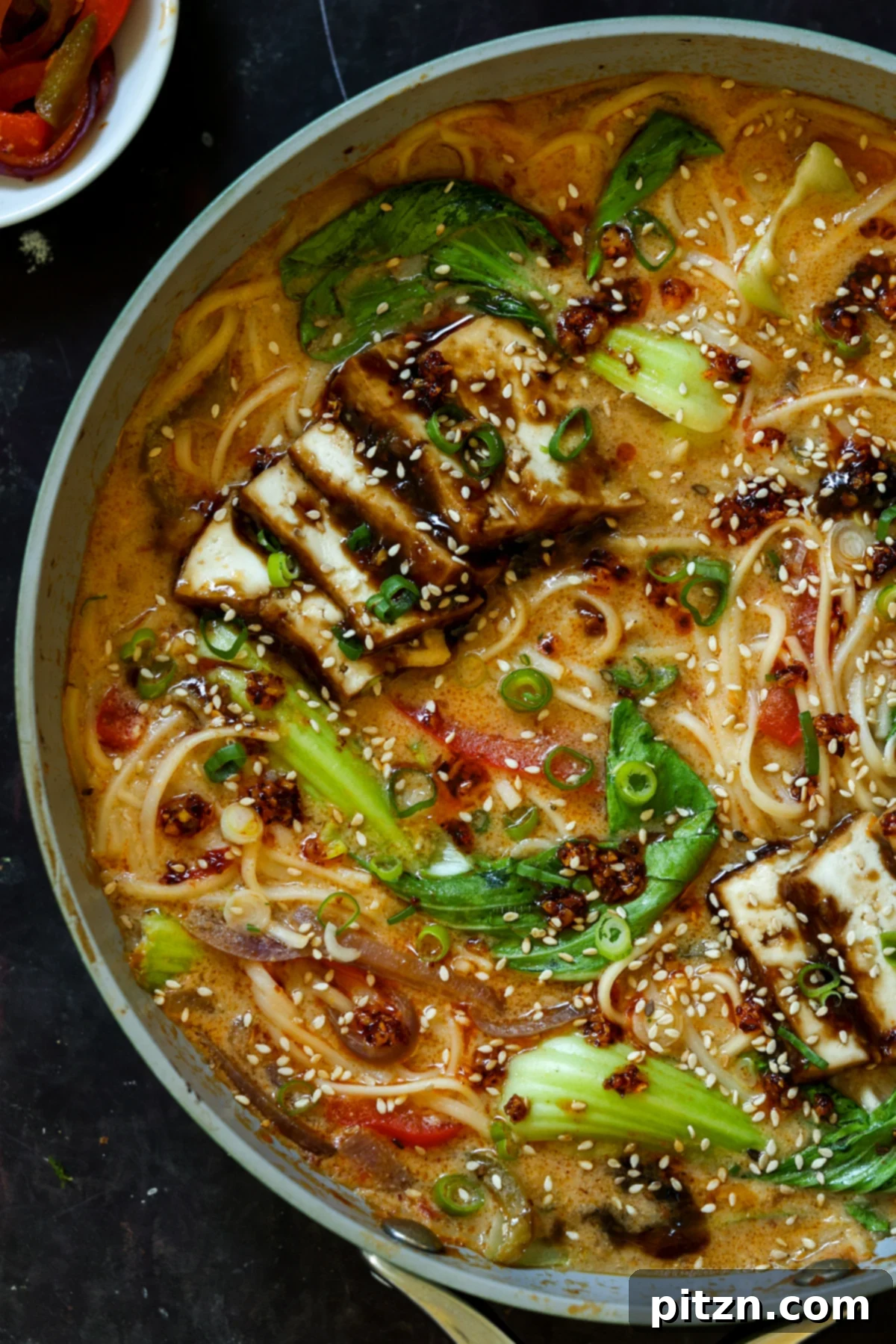 close-up view of a pan brimming with creamy tahini ramen, showcasing the textures of noodles, broth, and tofu