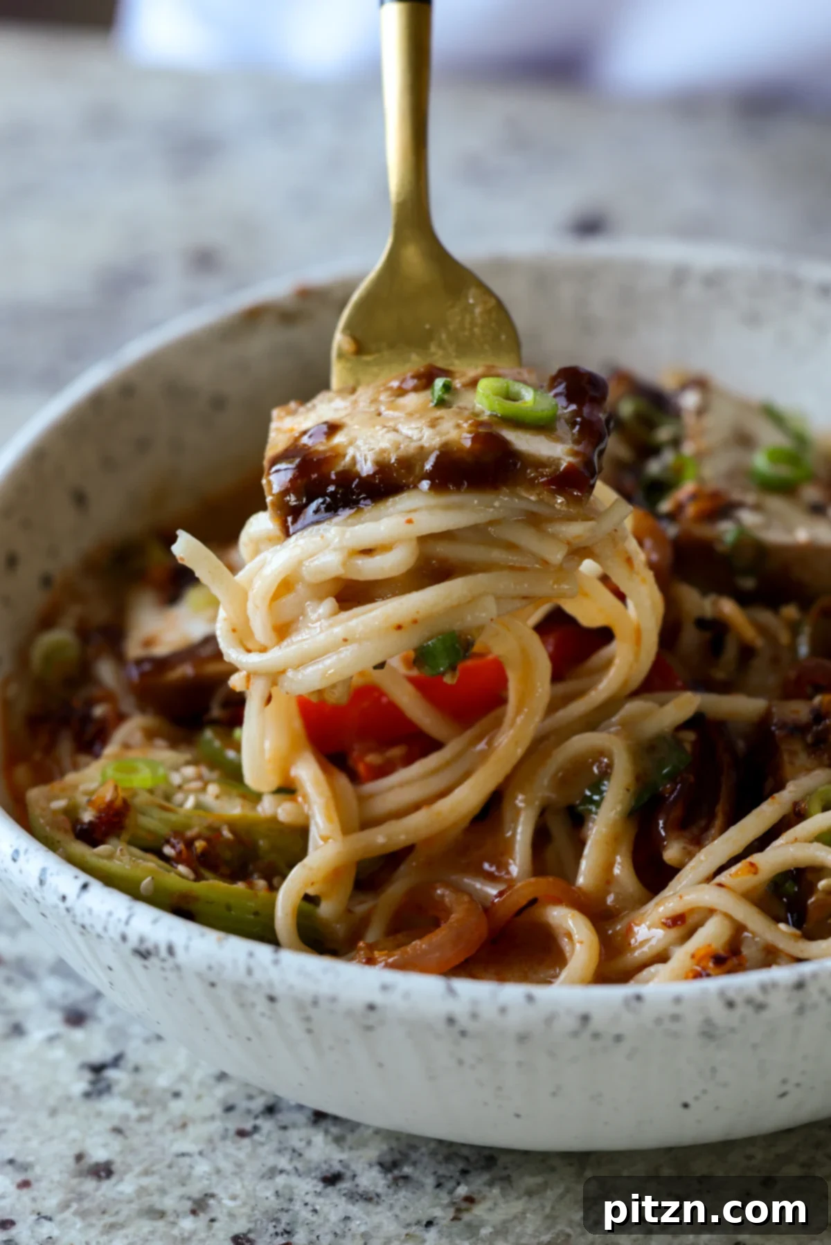 a fork holds a generous bite of ramen noodles and glazed teriyaki tofu, highlighting the rich texture