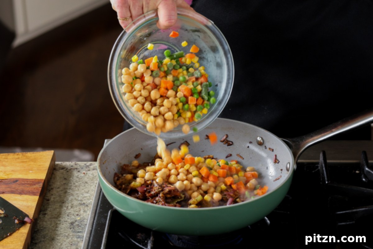Adding chickpeas and mixed vegetables to the skillet.