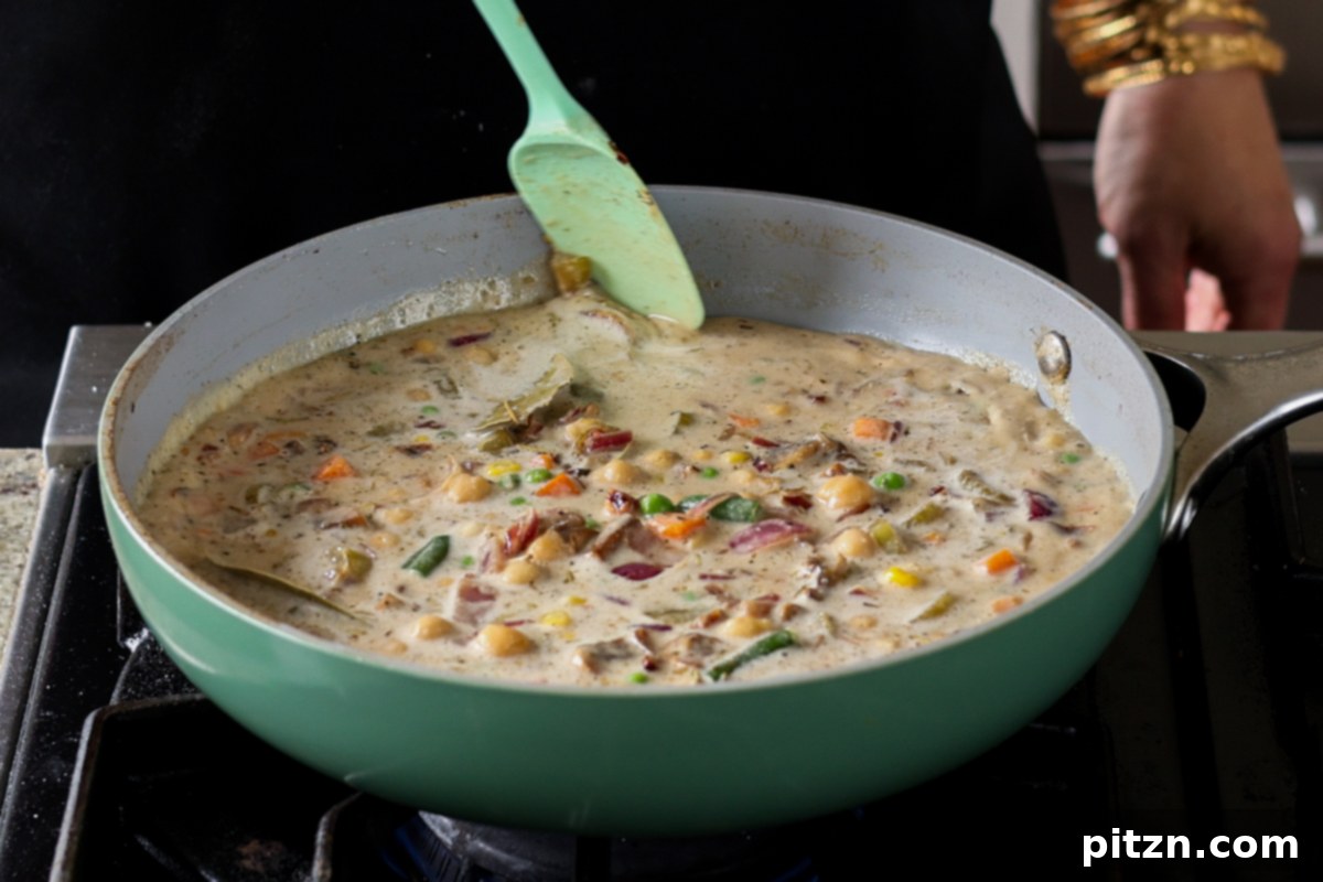 The pot pie filling simmering in the pan before it has fully thickened.