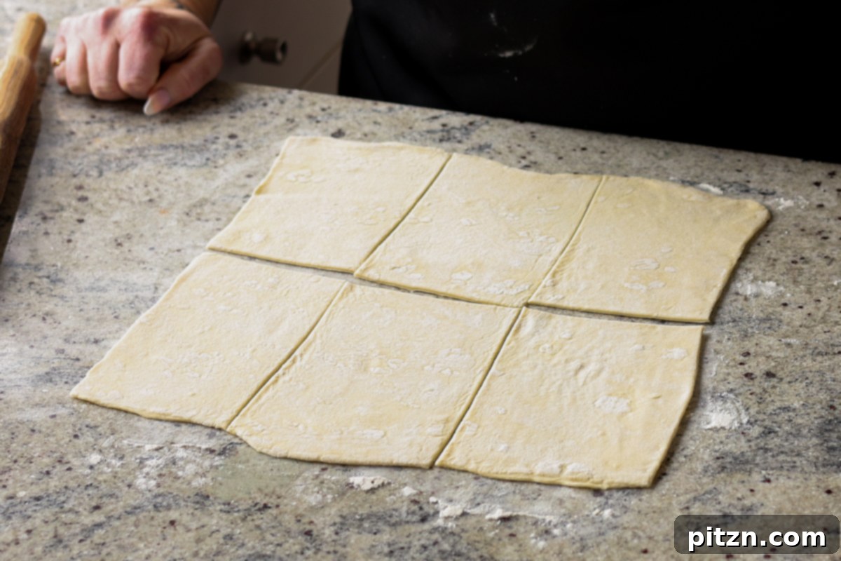 Cutting puff pastry into square shapes using a pizza cutter.