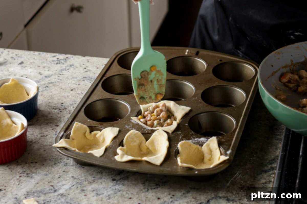 Filling the puff pastry-lined muffin tin with the cooled pot pie filling.