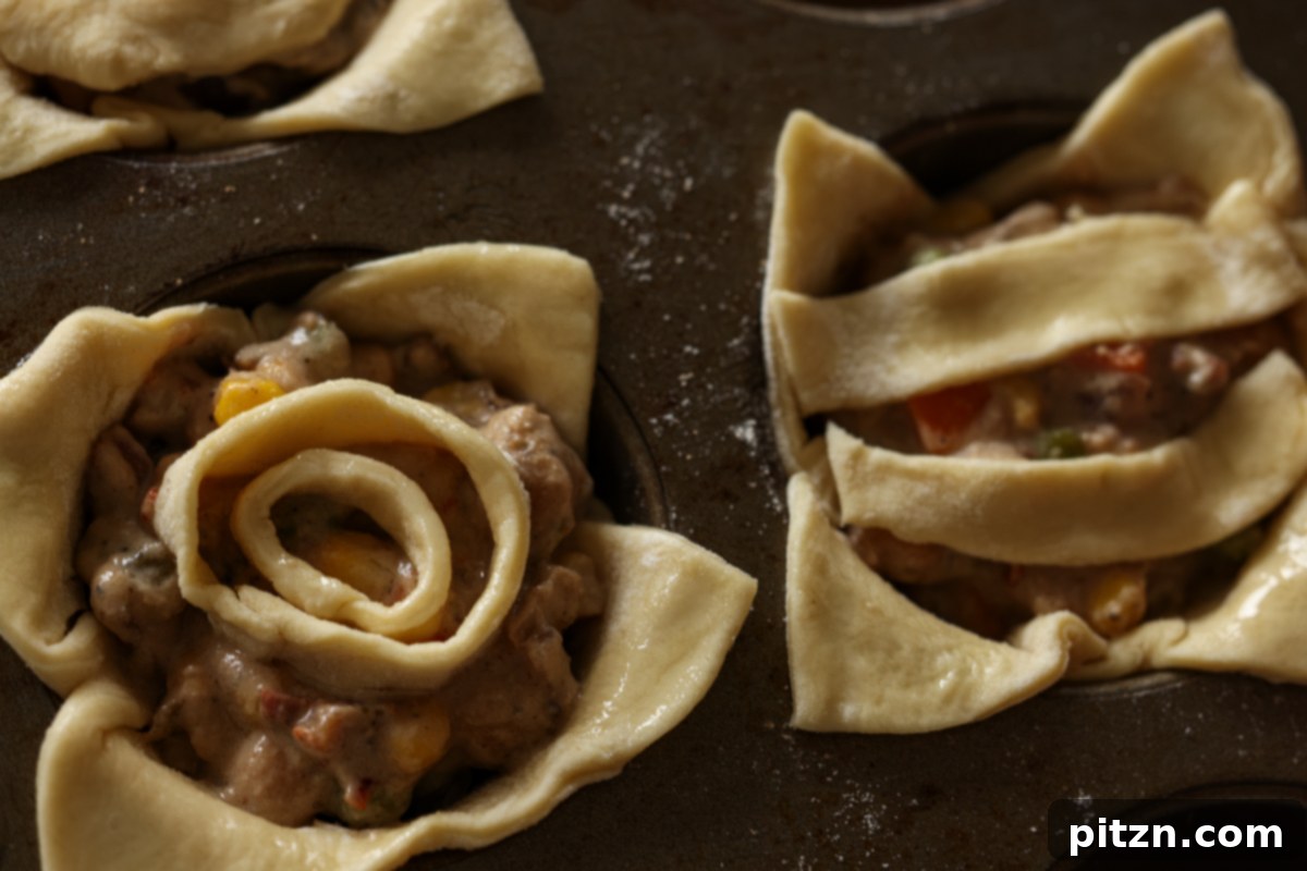 Mini pot pies in a muffin tin before baking, topped with puff pastry designs.