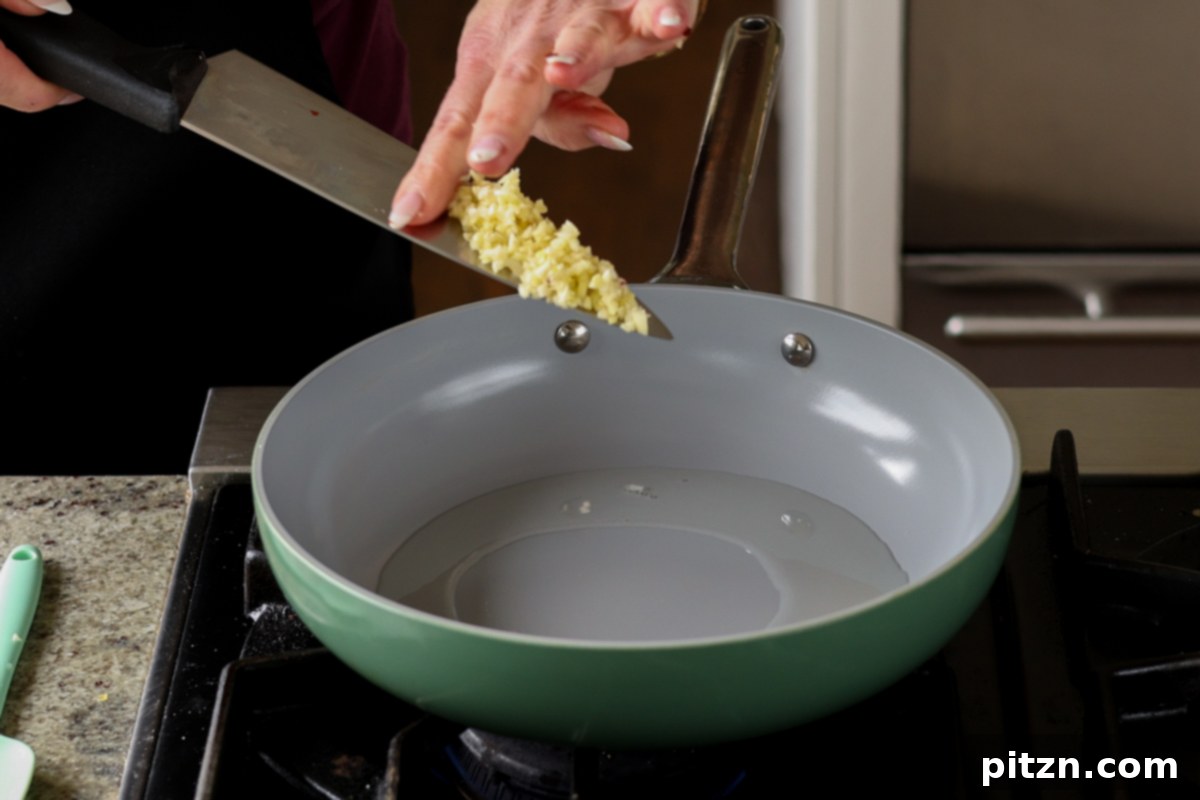 Adding chopped garlic to a hot skillet with oil.