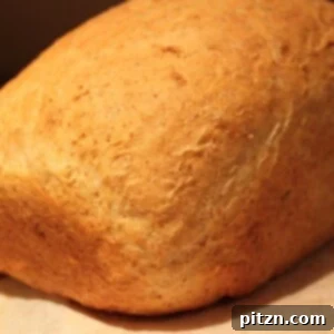 An olive oil sandwich loaf resting on a wooden chopping board, garnished with rosemary, awaiting slicing.