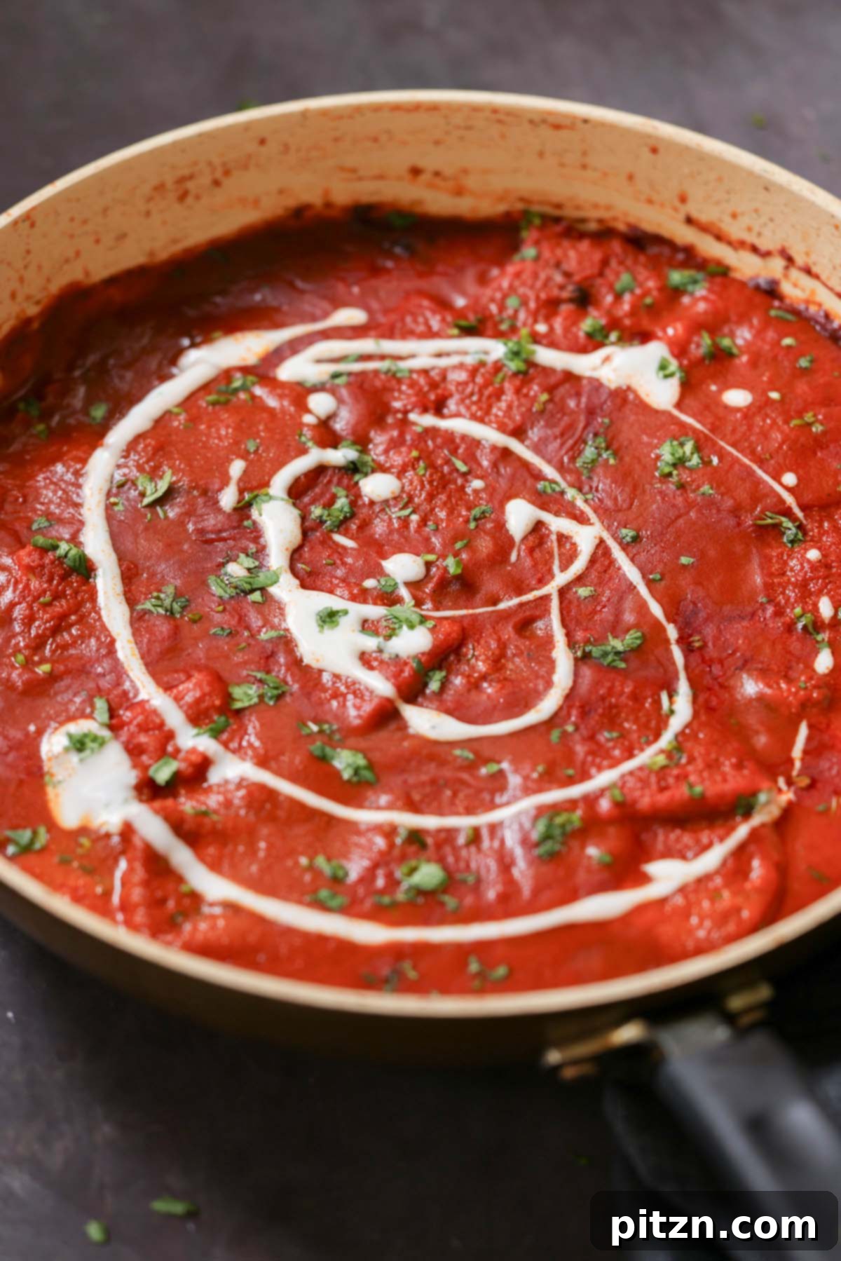 Pan of rich vegan Kashmiri Lal Tofu topped with a swirl of non-dairy yogurt and fresh cilantro