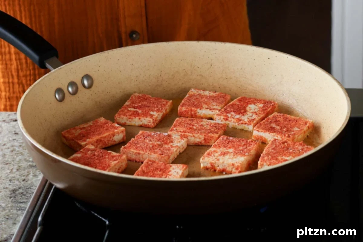 Uncooked, seasoned tofu pieces arranged in a hot skillet before pan-searing