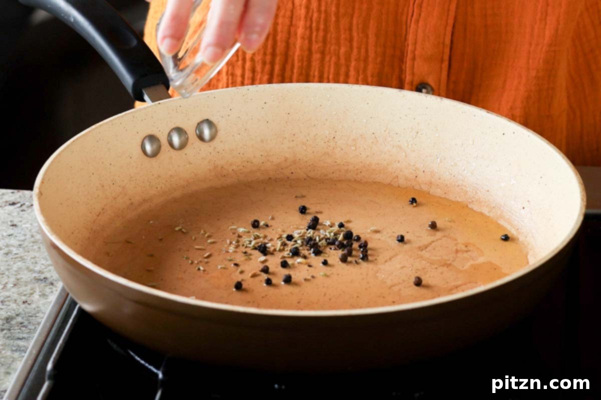 Whole fennel seeds and black peppercorns added to hot oil in a skillet