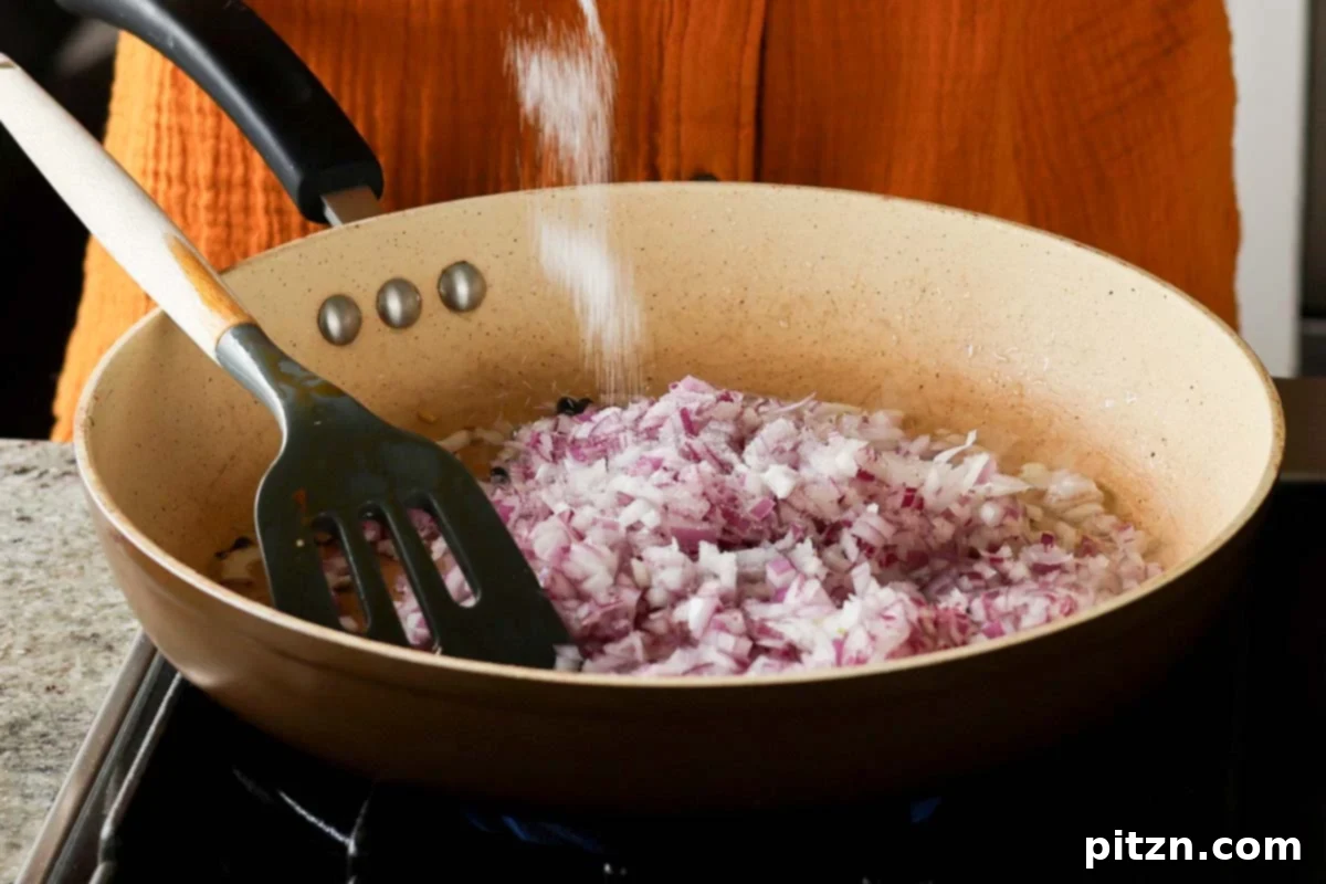 Chopped red onions and salt added to the skillet with whole spices, beginning to sauté