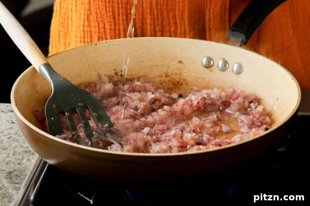 A hand adding a splash of water to the sautéing onions in the pan