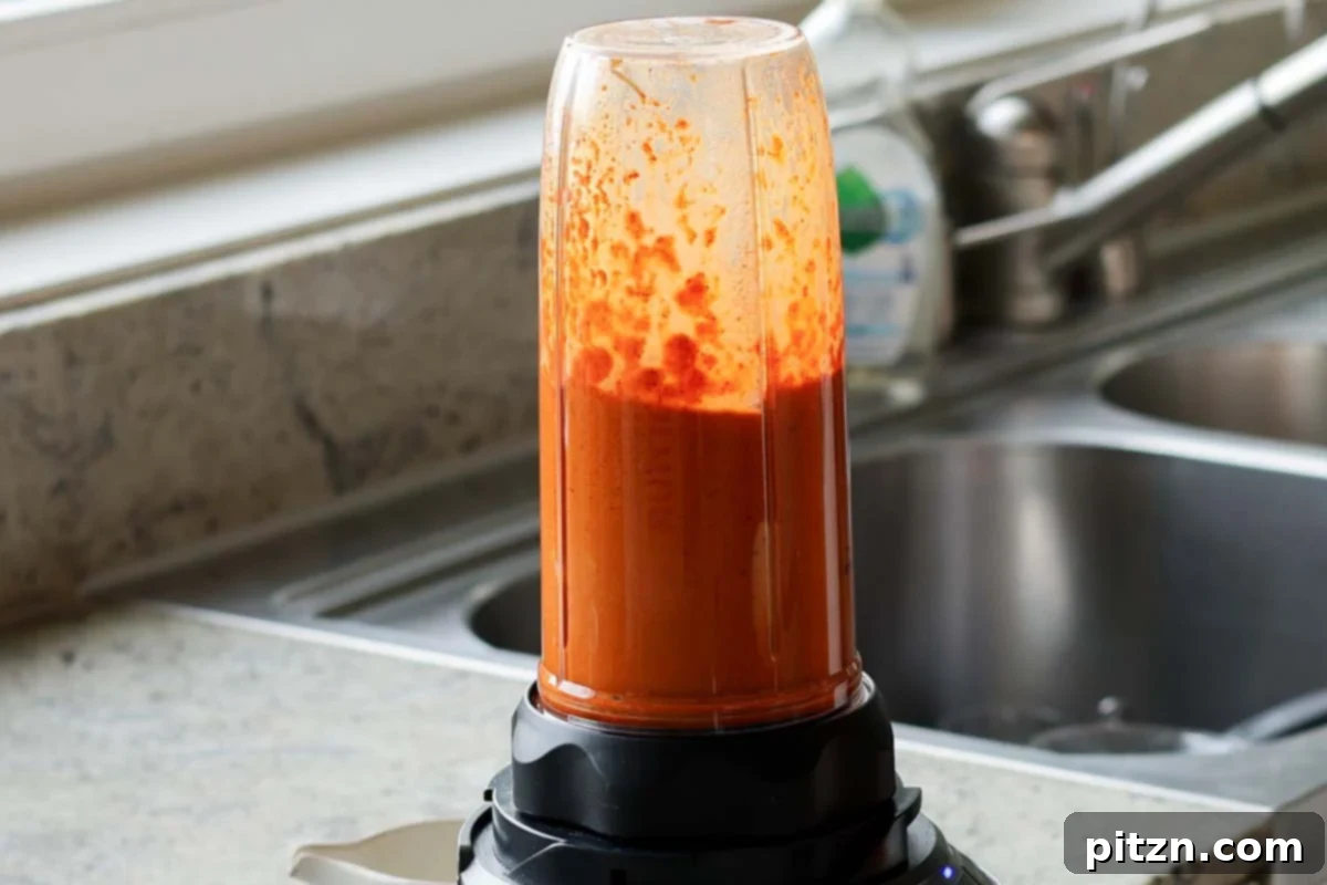 Close-up of a smooth, vibrant red tomato curry sauce in a blender after processing
