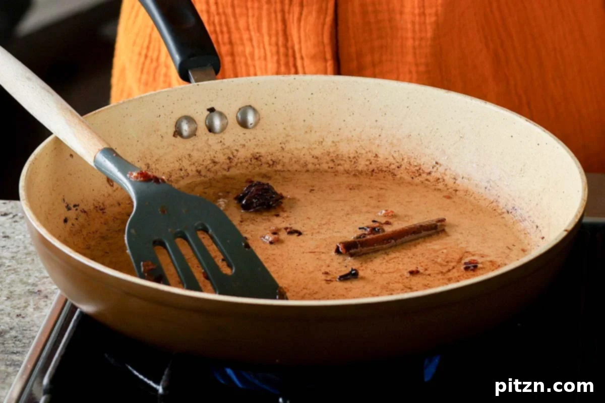 Black cardamom, cloves, and cinnamon stick added to hot oil in a skillet to temper